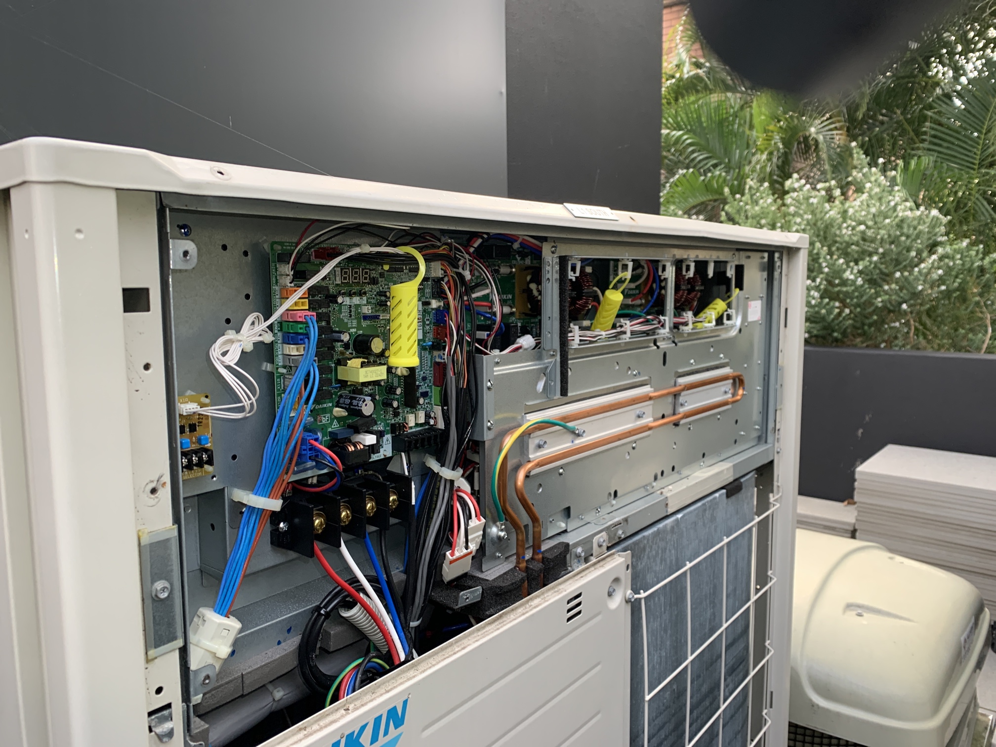 Daikin repairs Gold Coast specialist checking electrical components inside an outdoor Daikin air conditioning unit