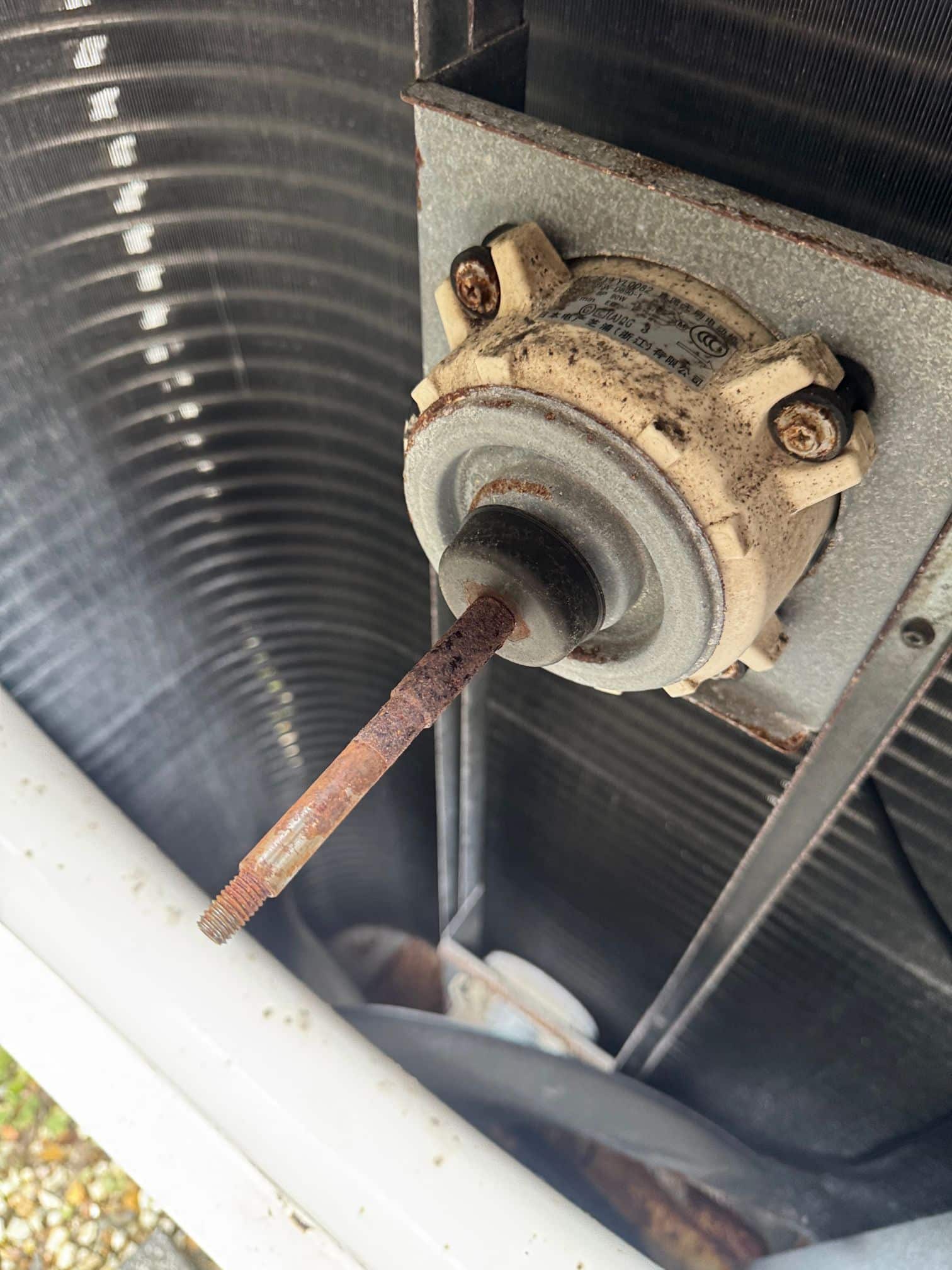 Air conditioning maintenance Gold Coast technician checking fan motor rust in an older outdoor unit