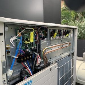 Daikin repairs Gold Coast specialist checking electrical components inside an outdoor Daikin air conditioning unit